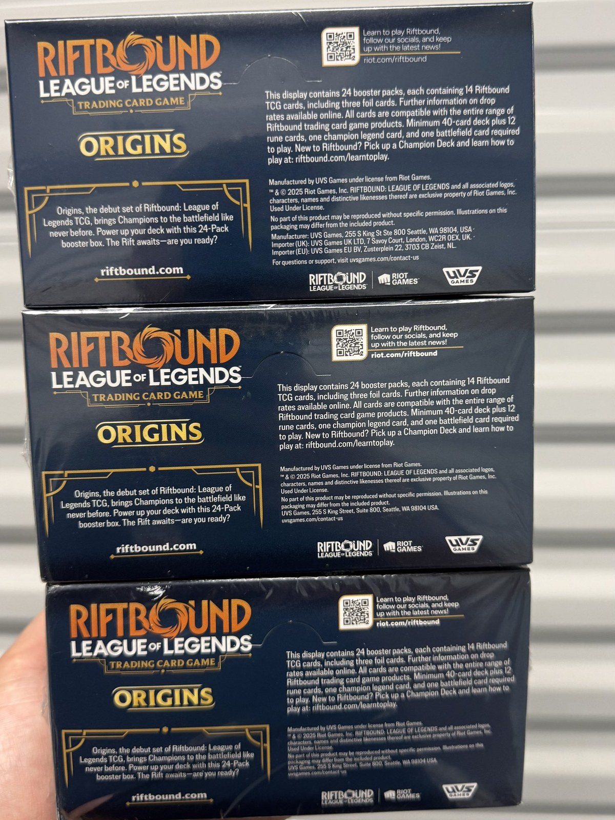 Three Riftbound Origins booster box back panels compared: the top box shows regular-weight text and an importer address block, the lower two show bold text with no importer block