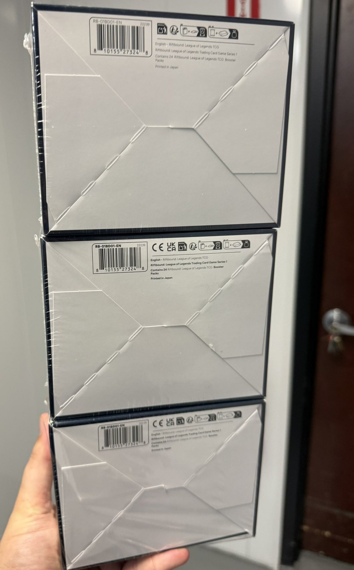 Bottom panels of three Riftbound Origins boxes: the top box lacks CE and UKCA marks and prints RB-01BD01-EN in light type, the lower two show CE and UKCA marks in heavy type